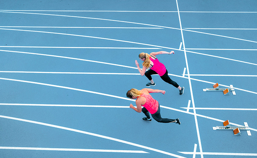 two women in pink running on blue track